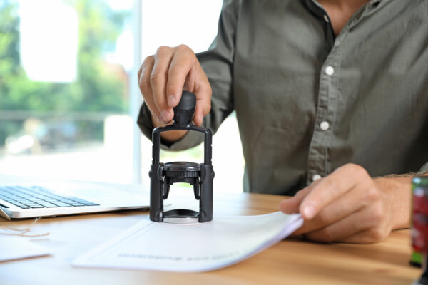 Male Notary Stamping Document At Table In Office, Closeup SBA 504 loan closing
